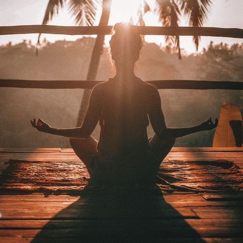 Woman meditating at sunset on a wooden deck.