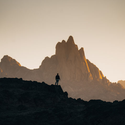 Silhouette of a person standing on a mountain peak at sunset