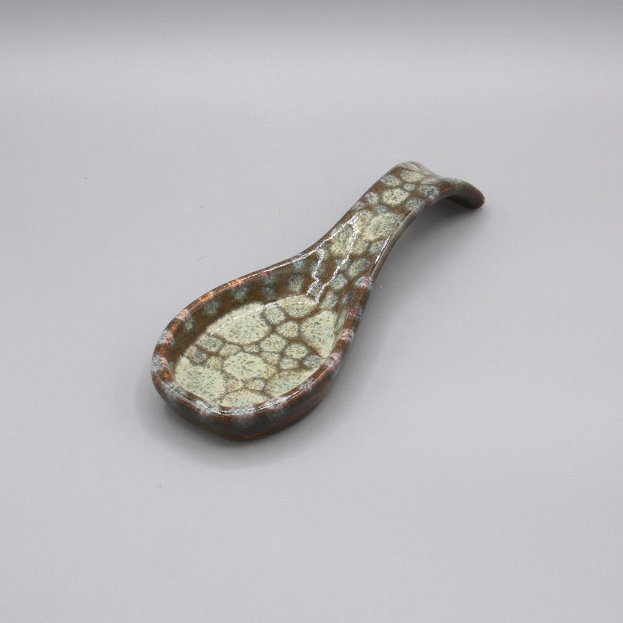 Handmade ceramic spoon rest with a brown glaze and creamy blue dot pattern, resembling stones beneath water.
