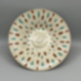 A wide ceramic bowl with a beige glaze, decorated with a radiating pattern of alternating brown and teal glaze runs.