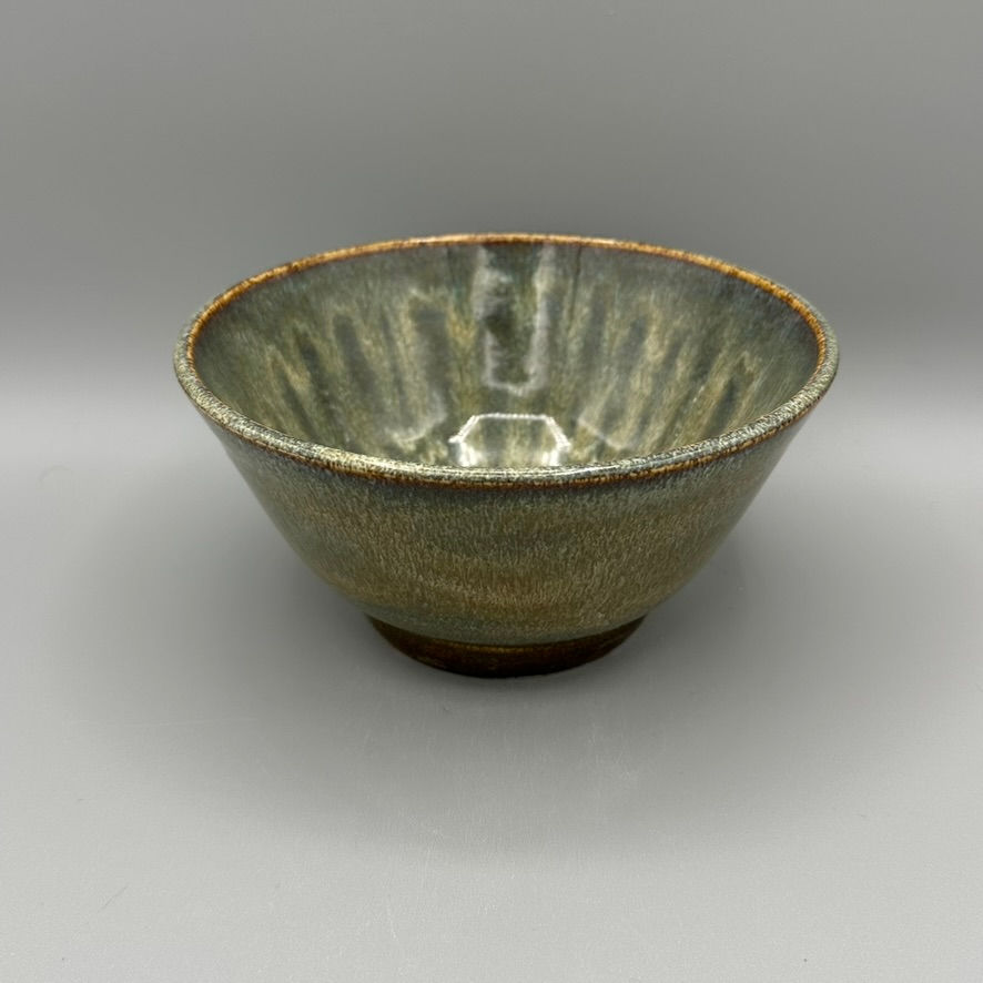 Handcrafted ceramic bowl with earthy green and brown glaze, featuring a textured, stone-like finish and a radial design.