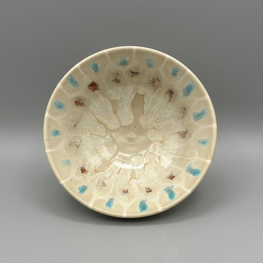 Small handcrafted ceramic bowl with a creamy glaze, featuring blue and red floral-like accents in a blooming radial pattern