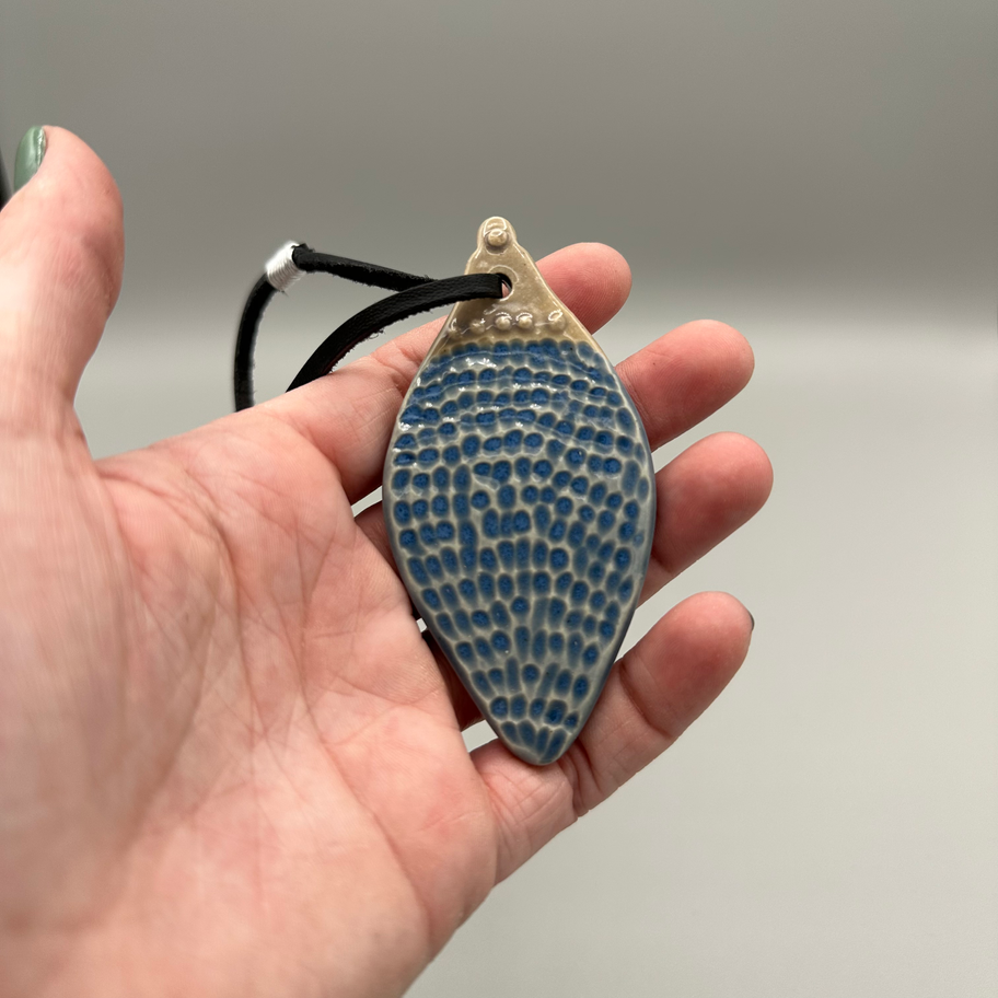 Hand holding a Rustic Teardrop Ornament in sky blue glaze with textured pattern and black cord.