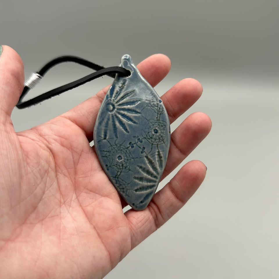 Hand holding a Vintage Lace Ornament in rustic blue glaze, featuring an intricate lace-imprint pattern and black cord