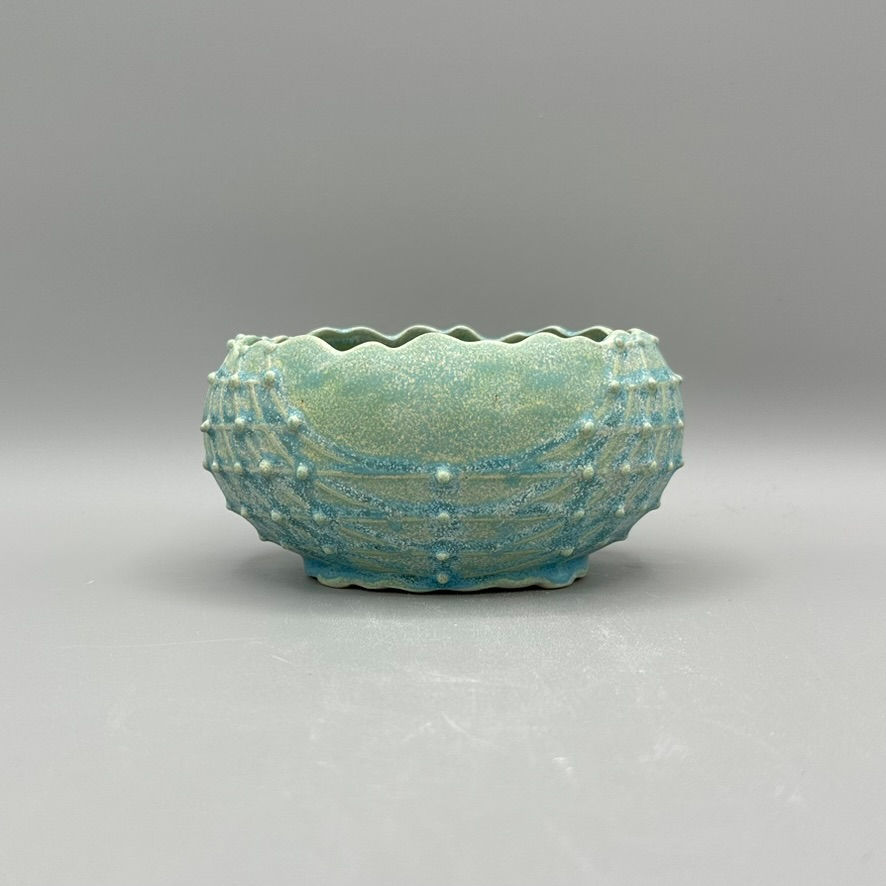 A blue-green ceramic bowl with a scalloped rim and raised dot and line texture around the exterior.