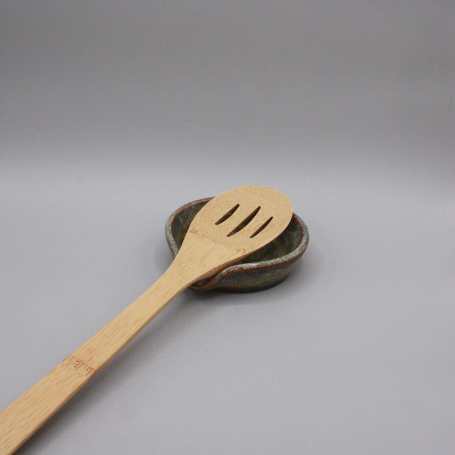Handmade ceramic spoon rest with a brown glaze and a creamy dip in the center, rounded with a curved edge.