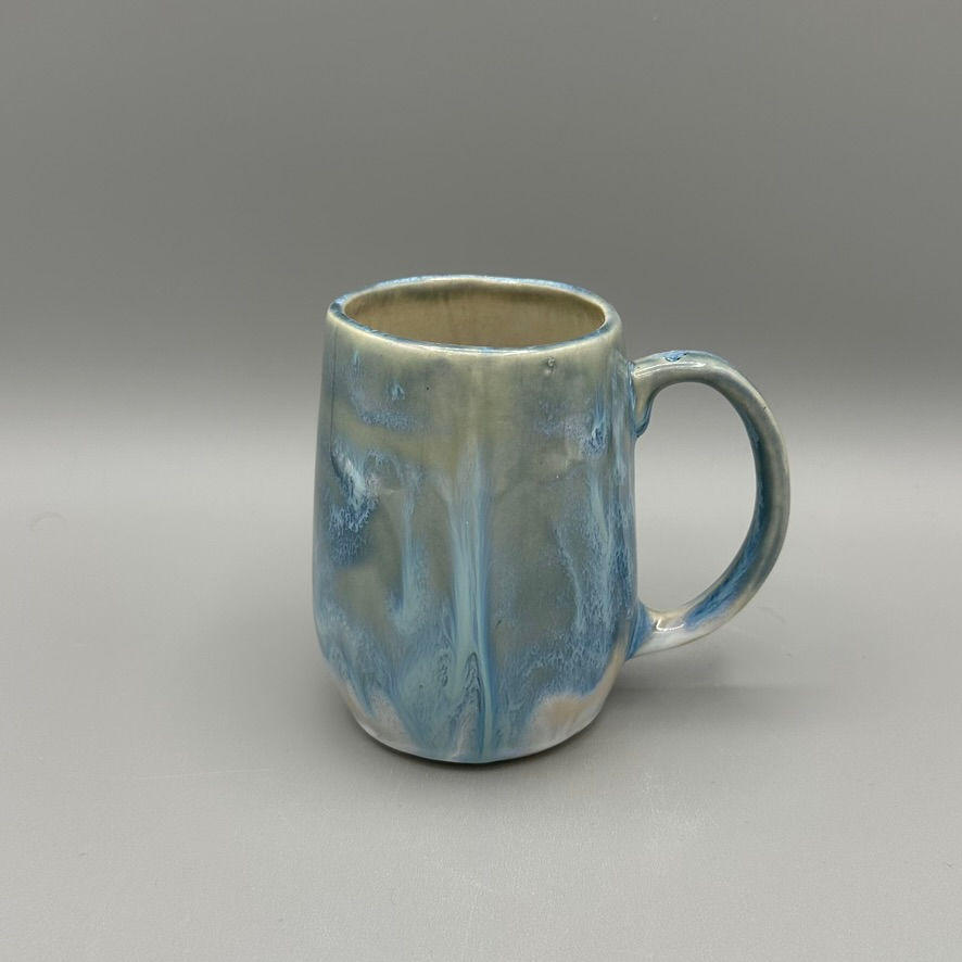 Handcrafted ceramic mug with a flowing blue and white glaze, featuring a rounded shape and comfortable handle.