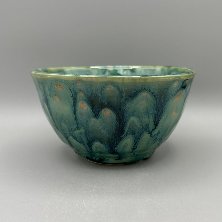 Handcrafted ceramic bowl with a glossy blue and mossy green glaze, featuring a radial, flower-like pattern in the center