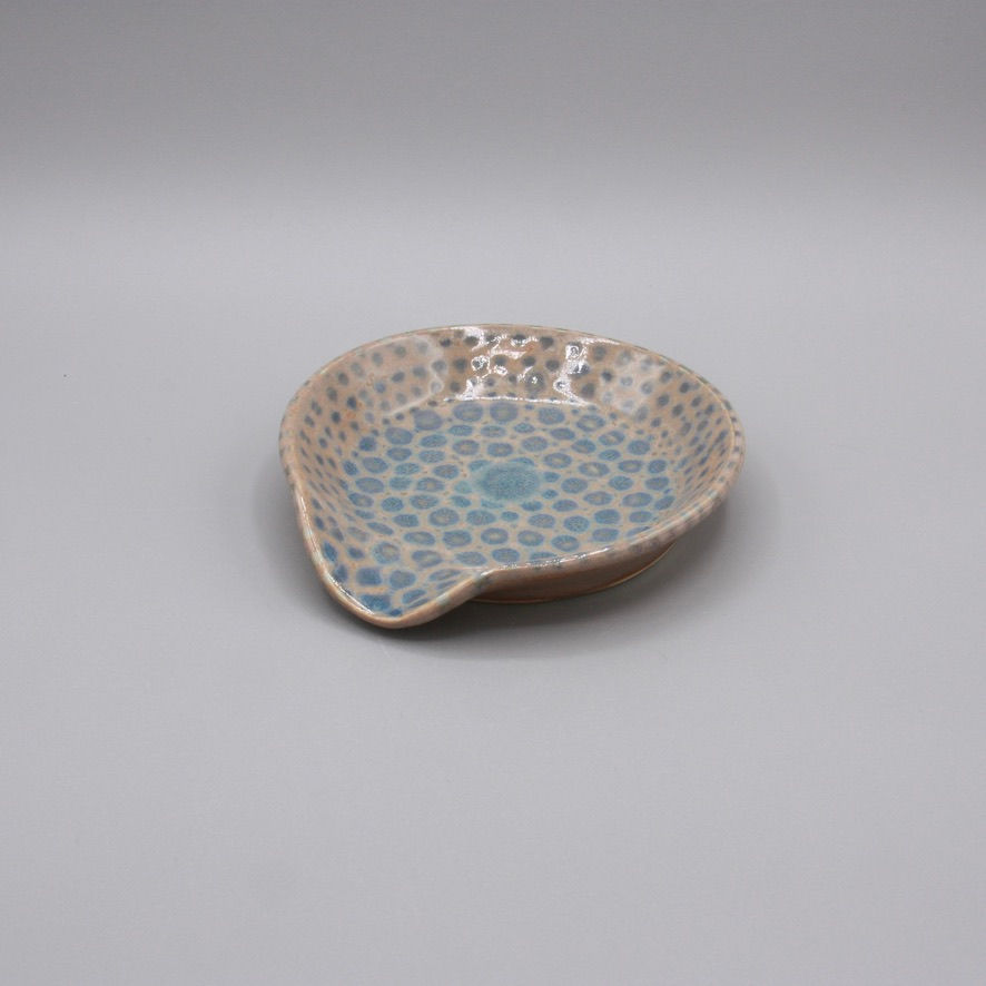 Handmade ceramic spoon rest with a brown and blue dot pattern. Rounded form with curved edge and organic, coastal texture.