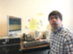 Photo of man seated at desk in front of a computer and phone.