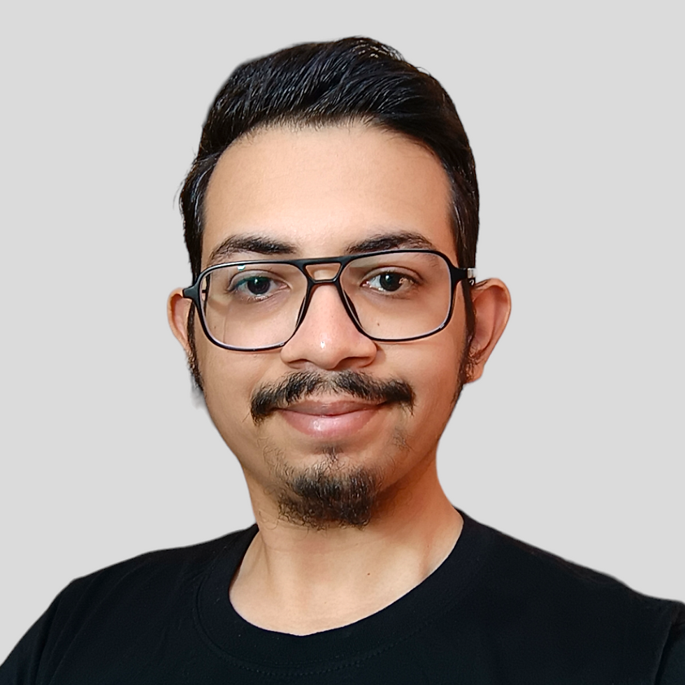 A person with glasses and facial hair smiles at the camera against a plain gray background, wearing a black shirt.