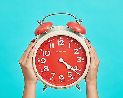 large-white-alarm-clock-with-orange-face-held-up-by-two-hands-against-turquoise-background