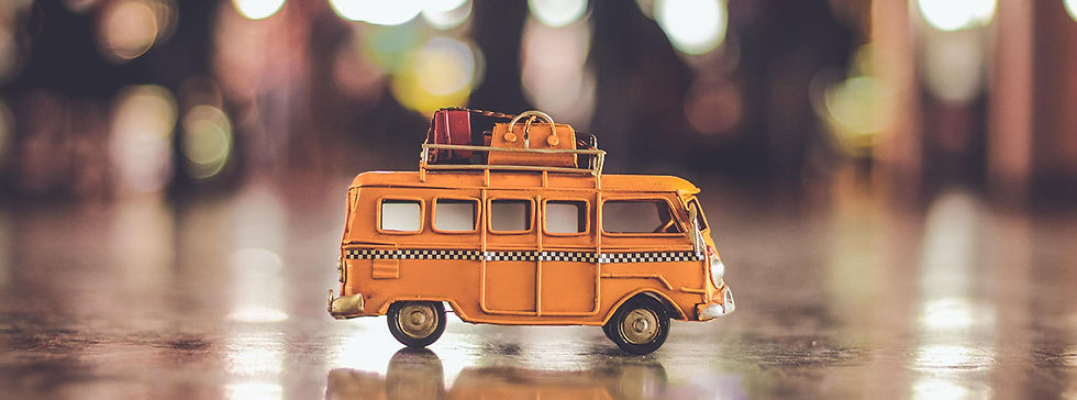 A toy yellow bus has luggage tied on the roof. Background is blurred. Image by Nubia Navarro (nubikini) on Pexels.