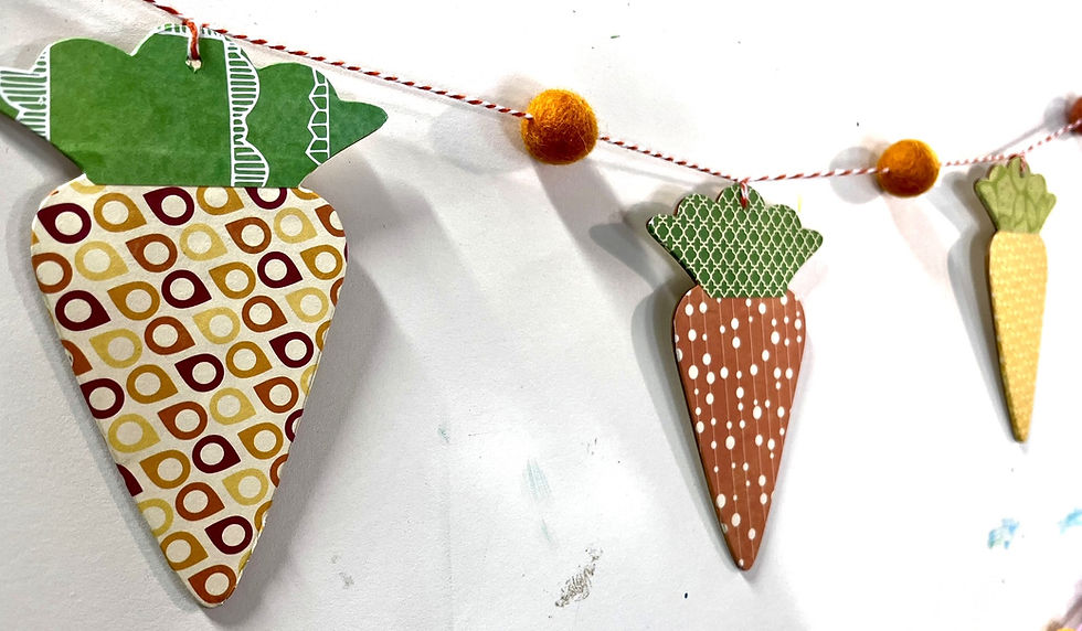 Easter banner with patterned scrapbook‑paper carrots separated by a small orange pom‑pom.