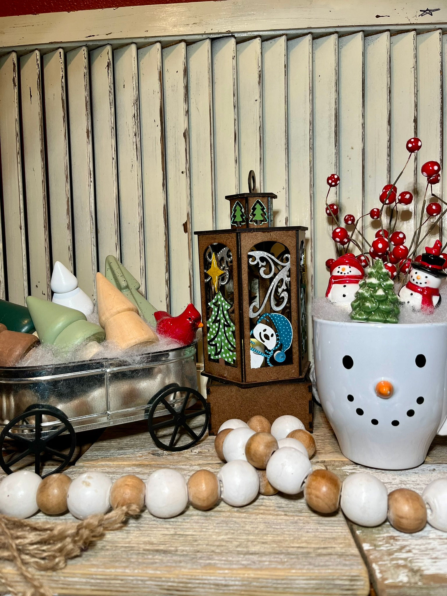 Painted winter lantern craft kit with laser-cut snowman and tree silhouettes, shown finished in holiday display