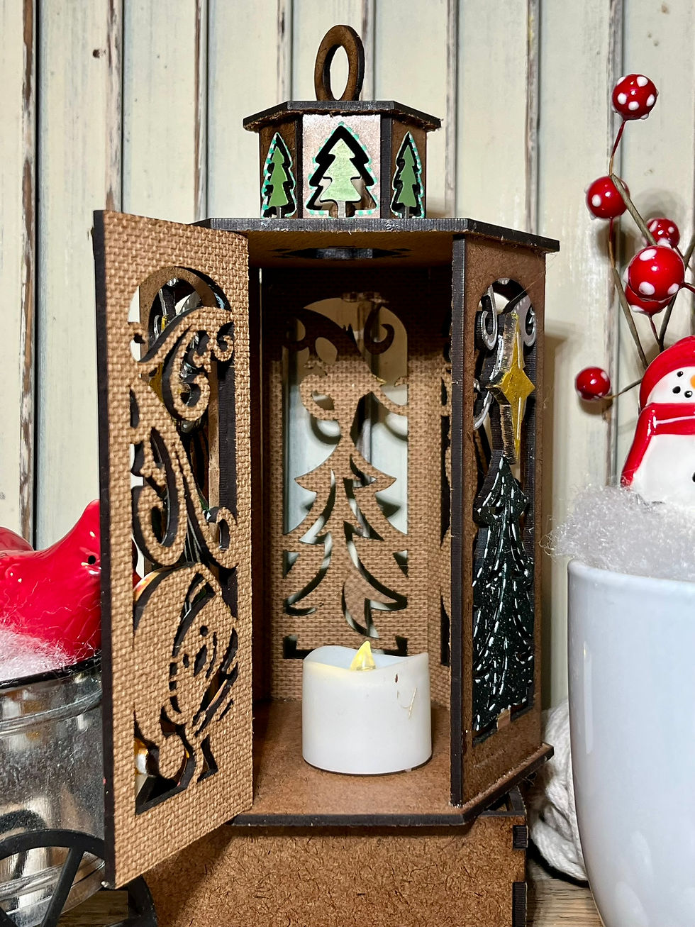 Thumbnail: Painted winter lantern craft kit with open doors revealing Christmas tree cutout and LED tealight, shown in festive holiday d