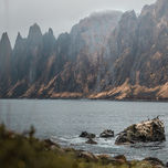 Felsenküste am Seeufer: Eine malerische Felsenküste, die in das ruhige Wasser eines Sees übergeht, umgeben von imposanten Bergketten.
