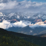 Bergpanorama mit Wolken: Ein atemberaubendes Panorama von schneebedeckten Bergen, die von Wolken umhüllt sind, was die Erhabenheit der Natur betont.

