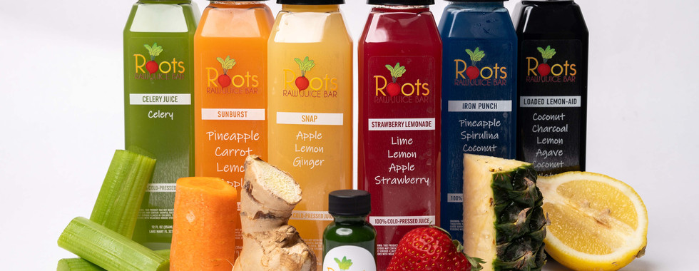 six bottles of raw fruit juice with their fresh ingredients in front of them