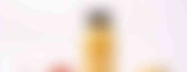 small bottle of ginger lemon juice shot on a white counter with the raw fresh fruit surrounding it .