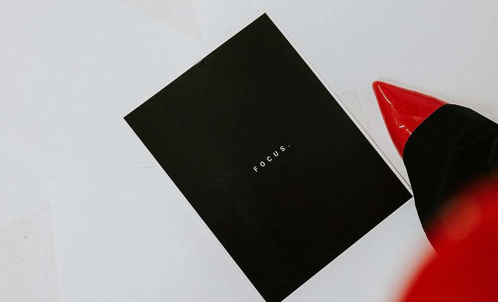 Overhead view of a black card with the word “FOCUS.” on a white surface, with red pointed shoes visible at the edge of the fr