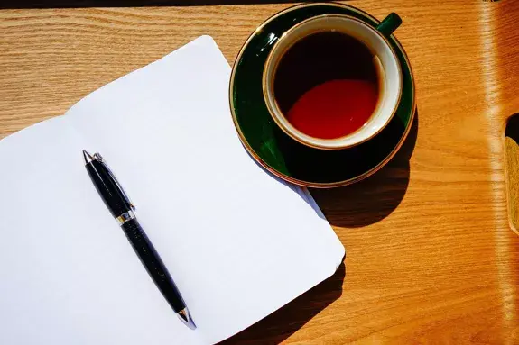 carnet ouvert avec un stylo et une tasse de thé