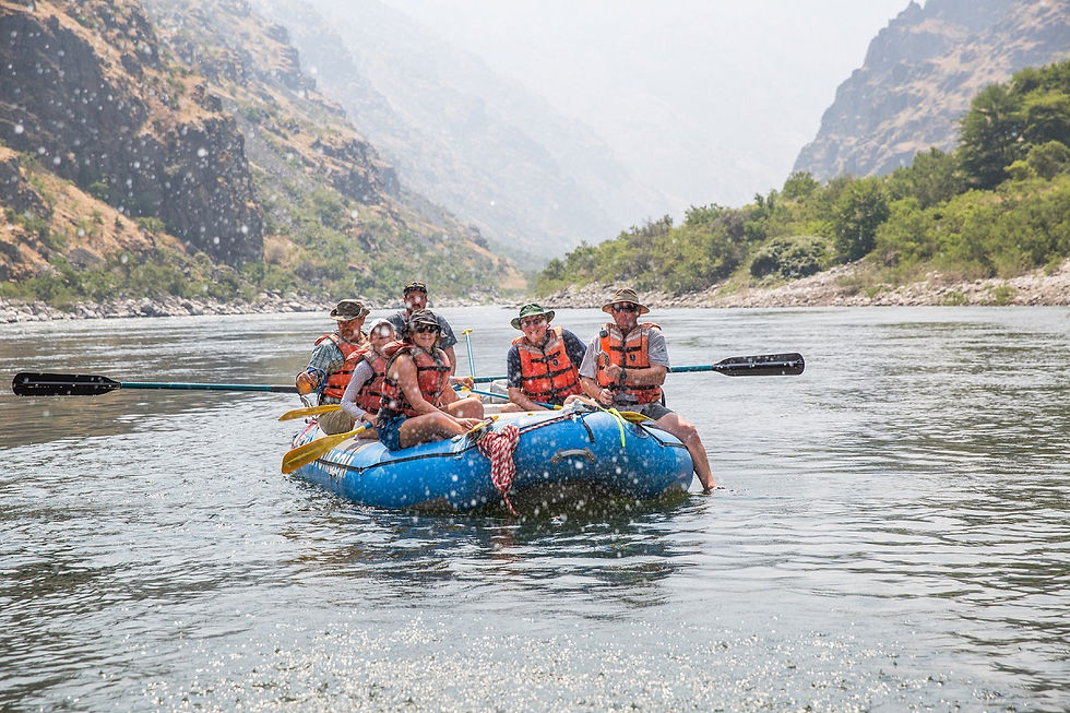 Group of people whitewater rafting on a calm river through a scenic canyon during an Idaho outdoor adventure tour.