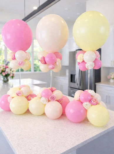 3 Pink, cream, and yellow balloon centerpieces with rose heads on a counter