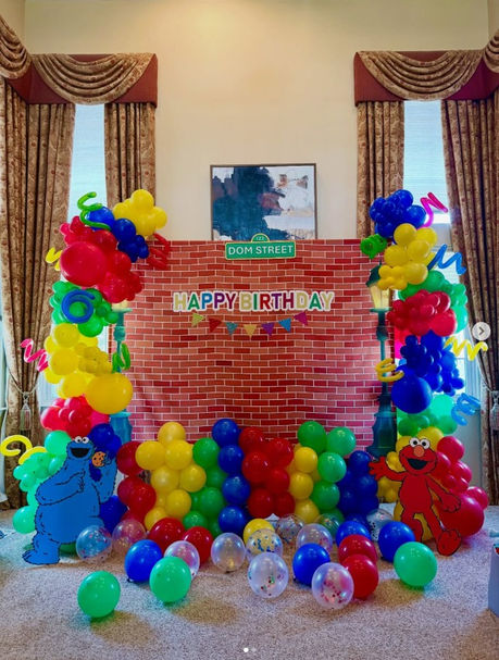 Colorful balloon arch and backdrop for a child's party that's sesame street themed with elmo and cookie monster cuouts