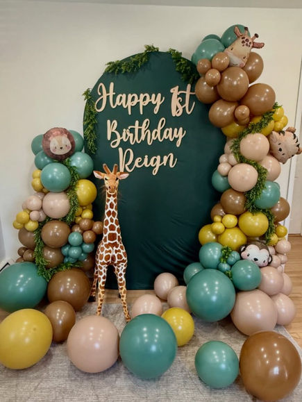 Happy 1st Birthday Reign forest green backdrop, giraffe, and balloons with specialty animal balloons and greenery