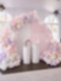 Pastel balloons in white pink and lavendar, 2 arch backdrop one white one pink that says "A Little Butterfly is On her Way", fresh flowers in the balloons, 2 white fluted pedestals one with a butterfly on top the other with a floral arrangement