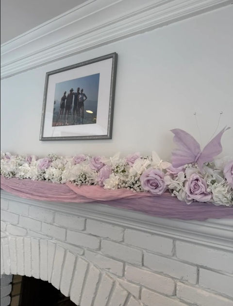 Fireplace mantle with lavender and white floral garland with lavender butterfly on the end