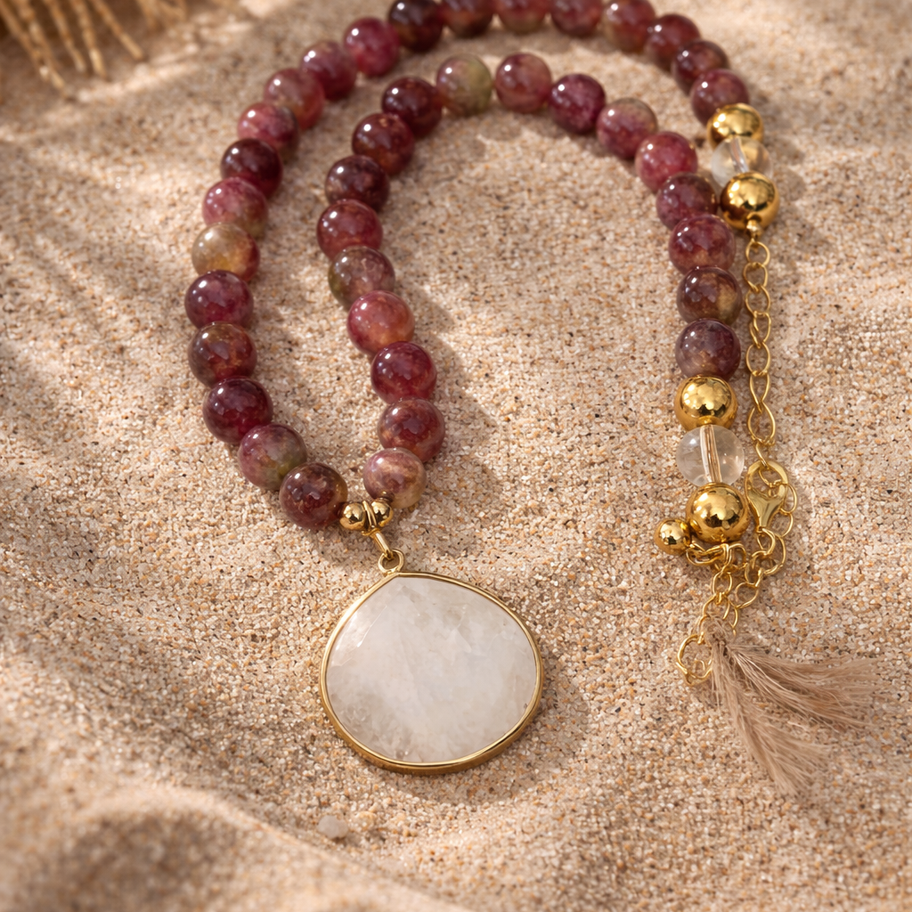 Pink tourmaline, 14k gold-filled beads and a clear quartz pendant laying in the sand