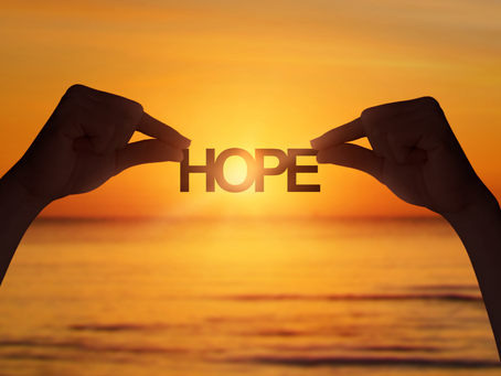 Silhouettes of two hands holding the word hope in front of a sunrise over water.