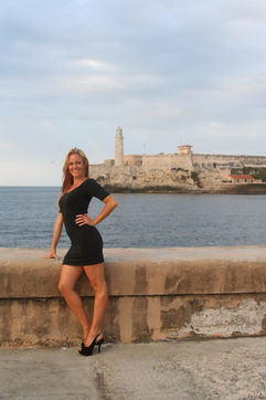 Kvinna i svart klänning poserar, stad och hav i bakgrunden, Malecon, Havanna. Hilderun Gorpe.