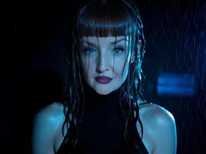 Close-up of a woman with wet dark hair and purple lipstick under blue rain-lit shadows, staring intensely at camera.