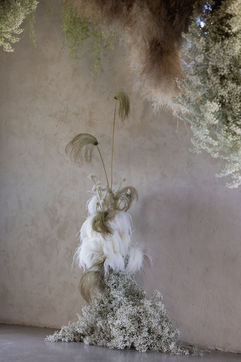 minimalist interior with suspended floral arrangements and a cluster of lit candles on the floor exudes an elevated sense of luxury. Natural light filters through a window above the hanging florals, creating an airy ambiance reminiscent of the Stones of the Yarra Valley.