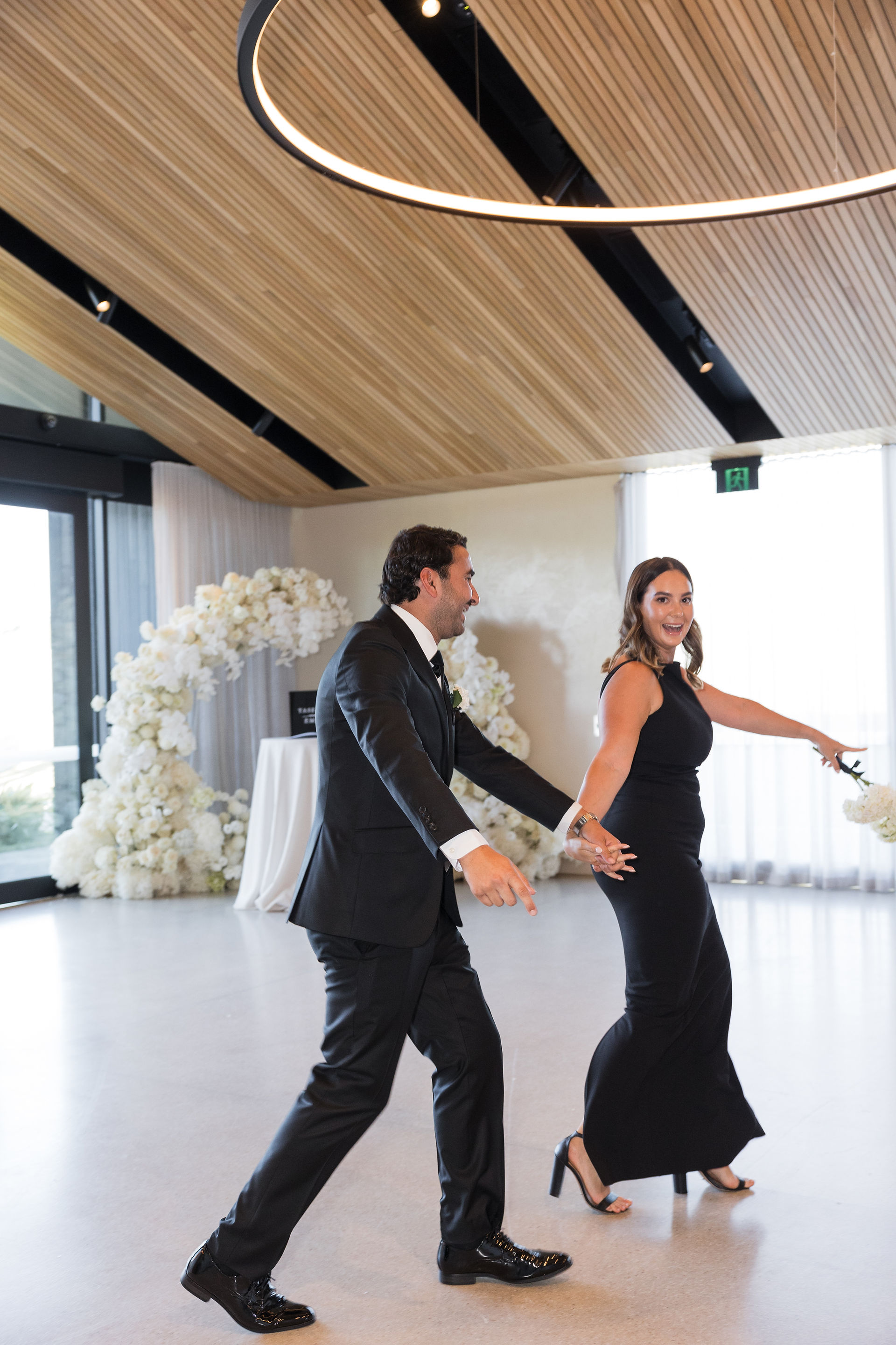 A white wedding reception backdrop decorated with lush white flowers and cascading strings of pearls.  Tall white candles line the base, illuminating the space.