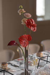 A close-up of a reception table in the evening, featuring cocktails, a white fabric runner, and glowing candles beside a minimalist floral centerpiece.