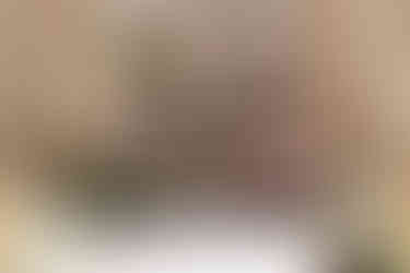 A beautifully decorated wedding altar features an abundance of pink, white, and purple flowers arranged in tall pillars flanked by classic columns. The elevated design exudes luxury, with a backdrop of a building with large windows and autumn trees adding to the enchantment.