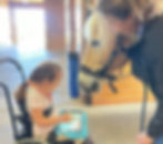 A girl in a wheelchair uses a communication device to chat with a horse and instructor.