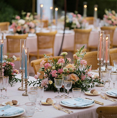 A table set up for a wedding with pink and blue taper candles and pink flower arrangements.