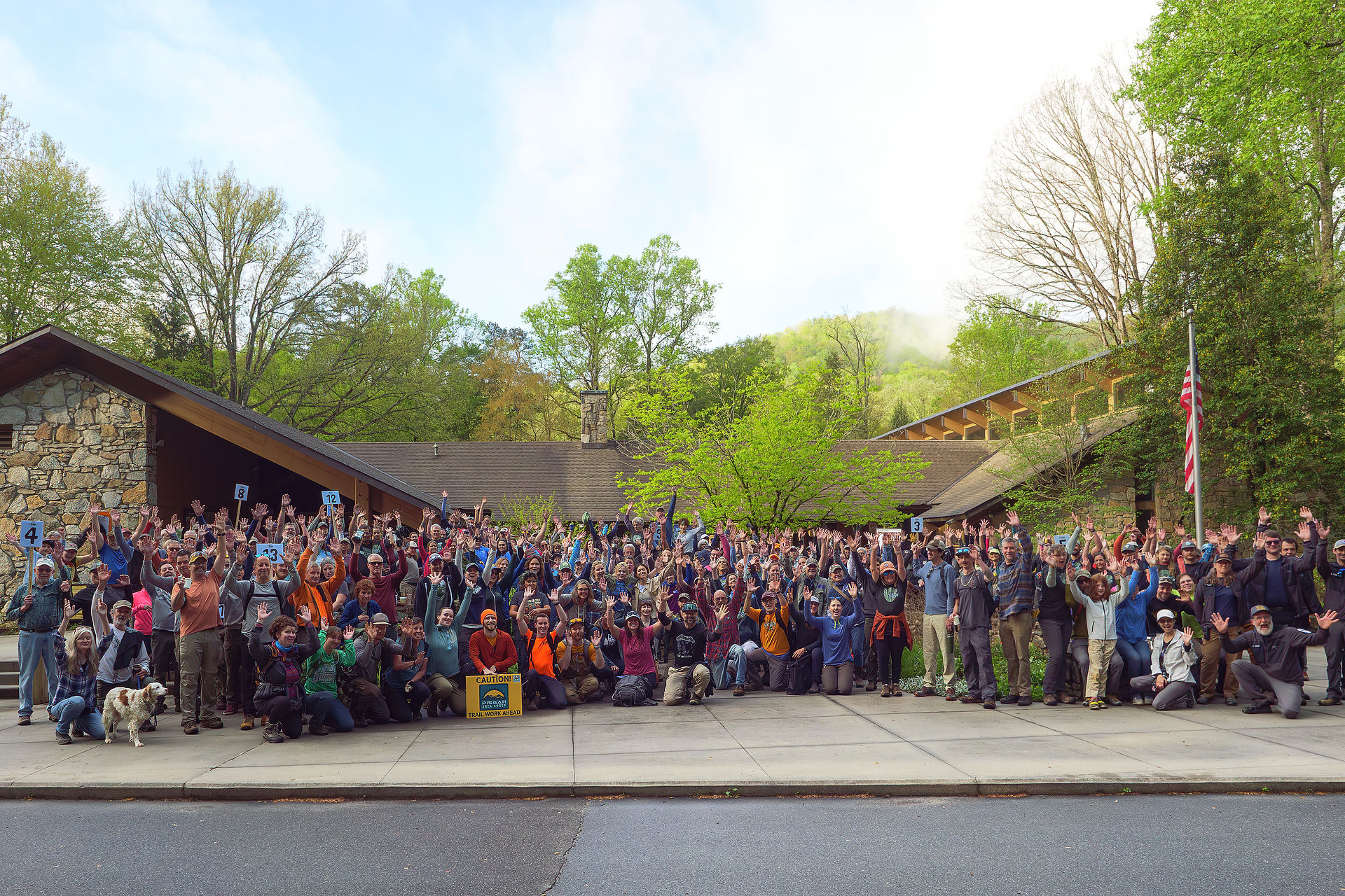 A group of forest conservation volunteers gathered in front of ranger station celebrating with their hands up.
