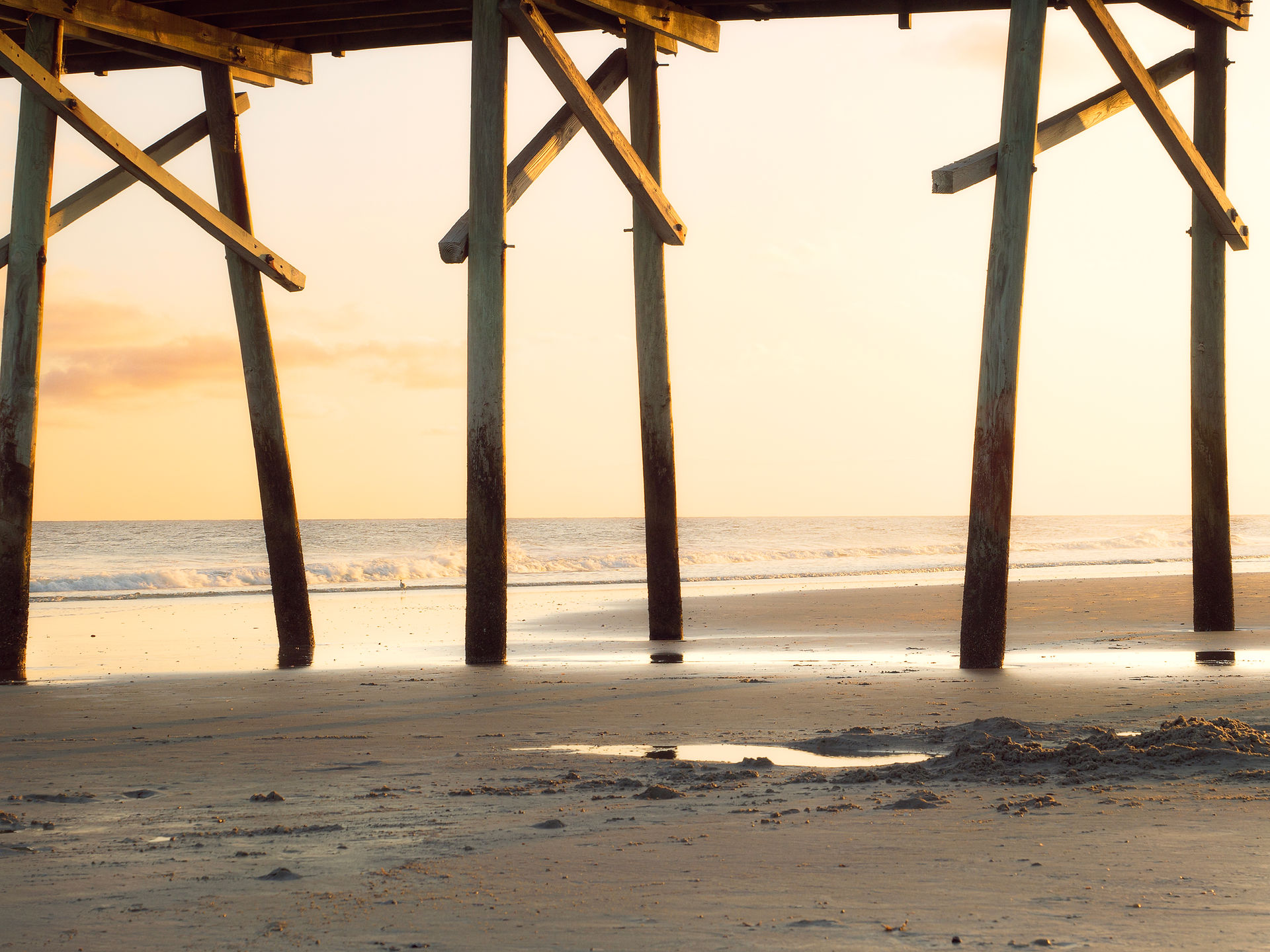 Sunset from under the pier on Atlantic Beach in Beaufort, NC overlooking the water.