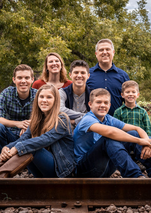 Family posing outdoors surrounded by trees during family photography session in Dripping Springs, Texas.