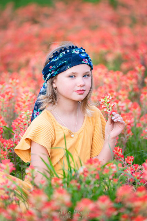 Girl standing in field of blooming orange wildflowers during spring outdoor photo session