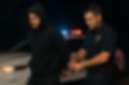 Police officer placing handcuffs on a man wearing a black hoodie beside a patrol car at night in Ocean City, Maryland-representing burglary and breaking and entering arrests