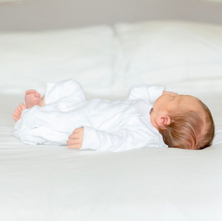 Newborn Photography Hertfordshire - Baby sleeping on a bed with a white outfit on.