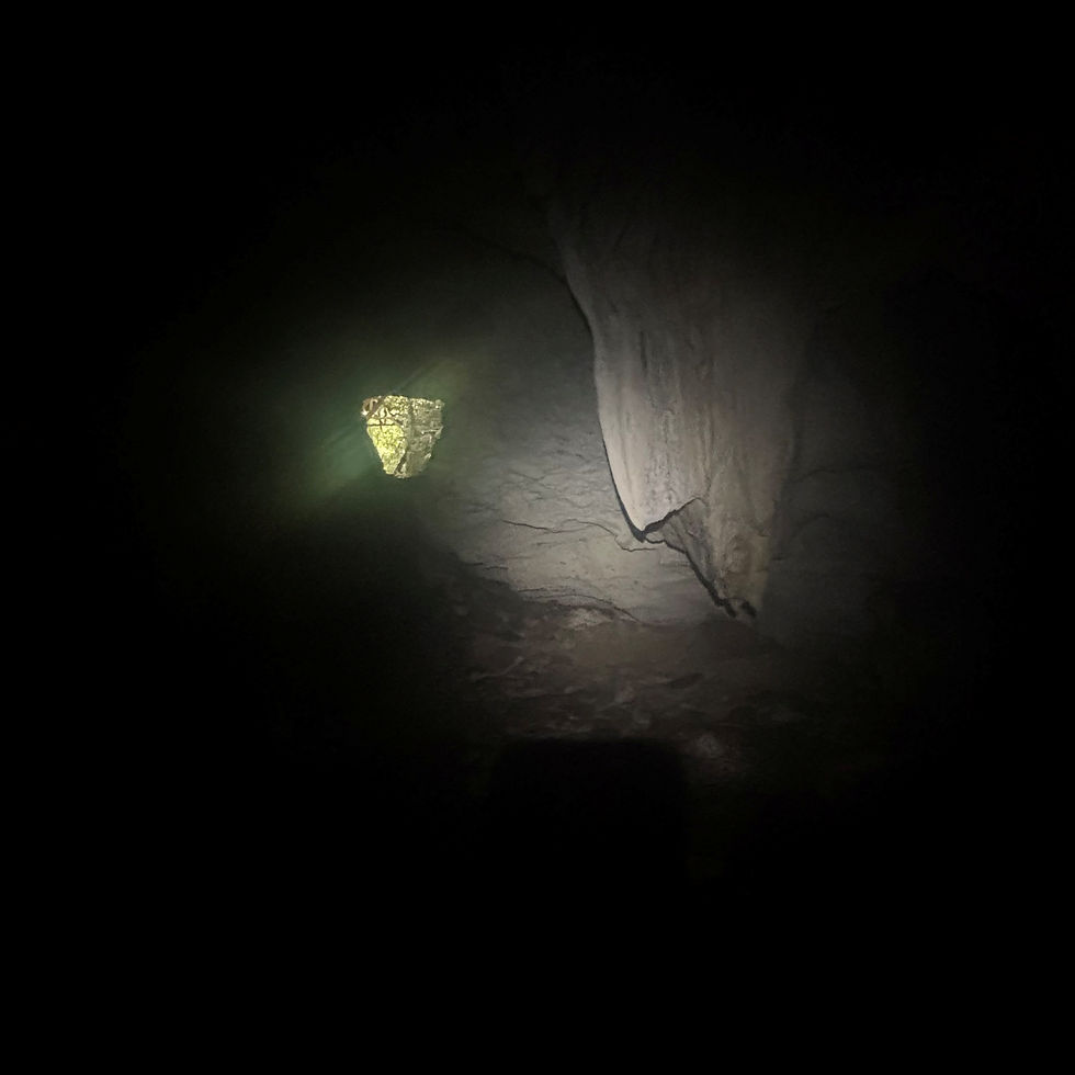 Dunkle Höhle mit Taschenlampenlicht auf Felswand und kleinem gelbgrünem Durchbruch; keine Personen sichtbar.