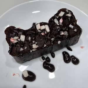 dark chocolate peppermint loaf with crushed peppermint candy on top on white plate dripping with chocolate sauce